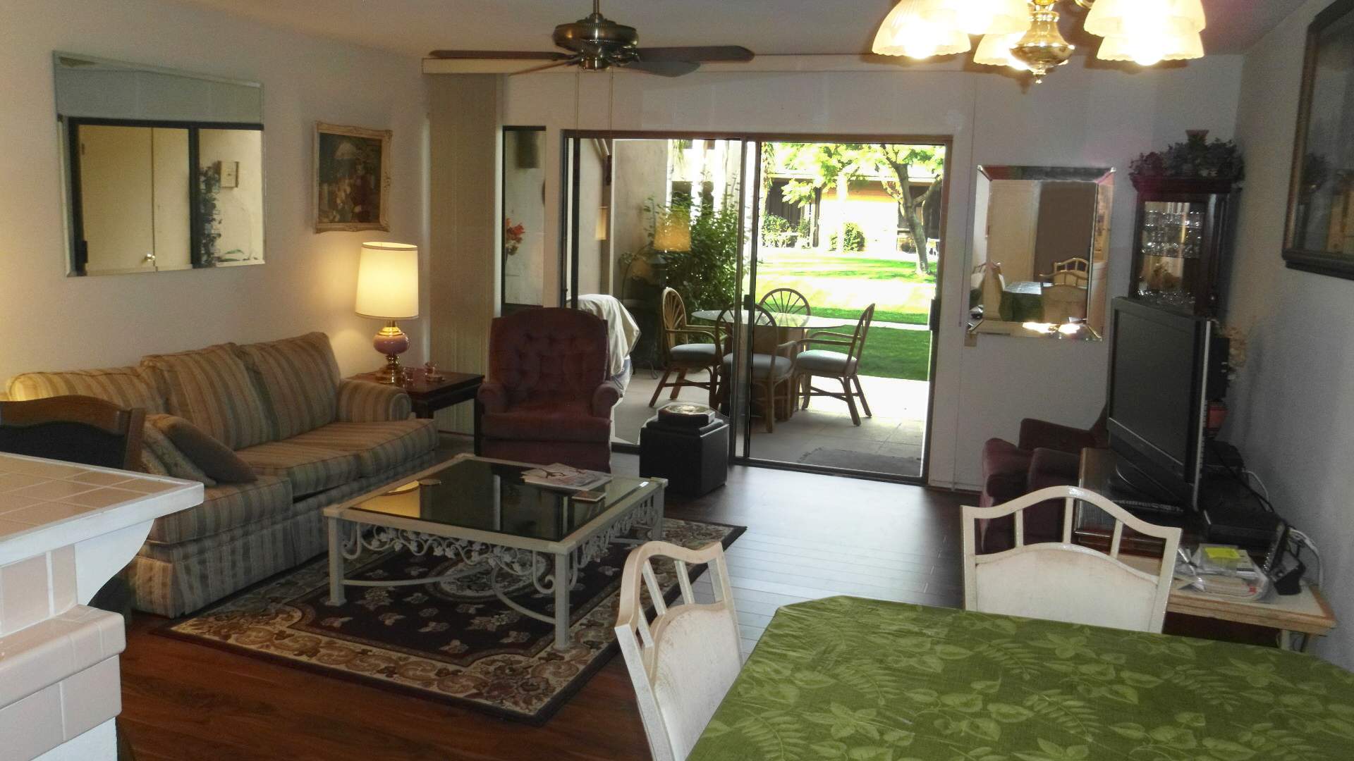 Living Room with Sofa, chair, coffee table, and TV.  Dining room talble and 2 chairs are in the front right and back patio can be seen through glass sliding doors.